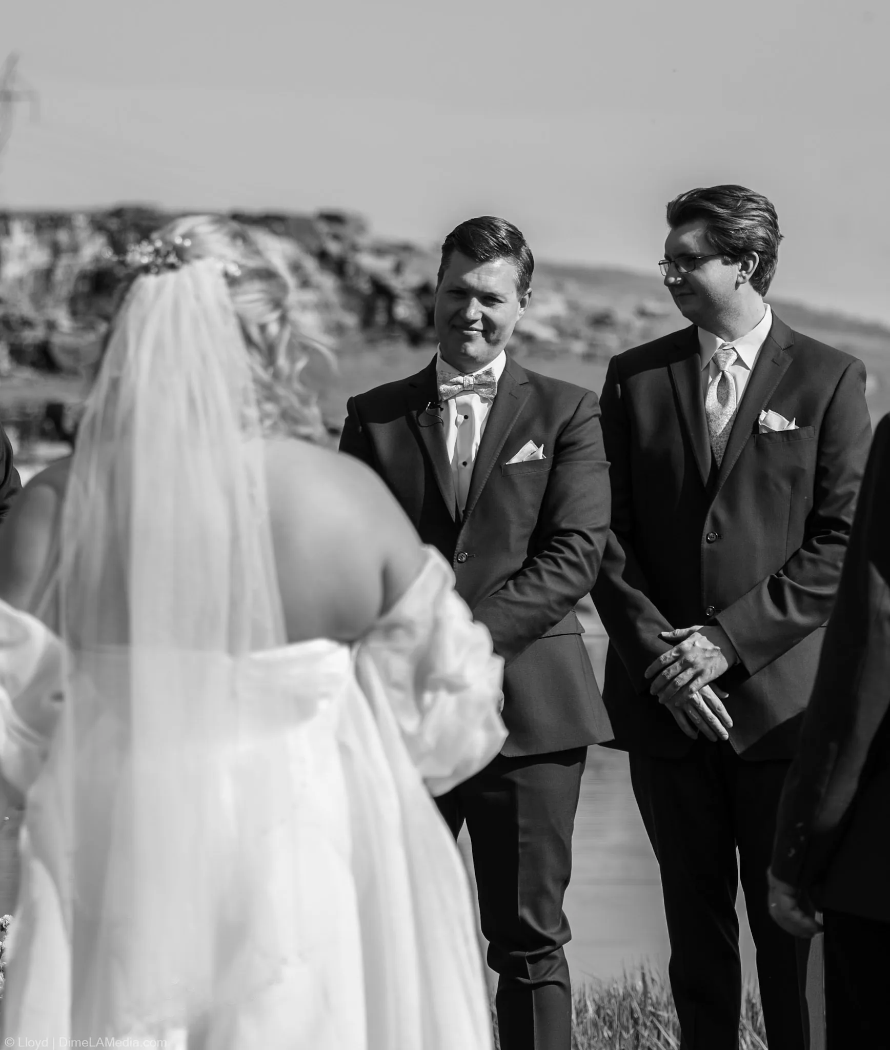 Black and white view over the bride's shoulder toward her groom during the ceremony