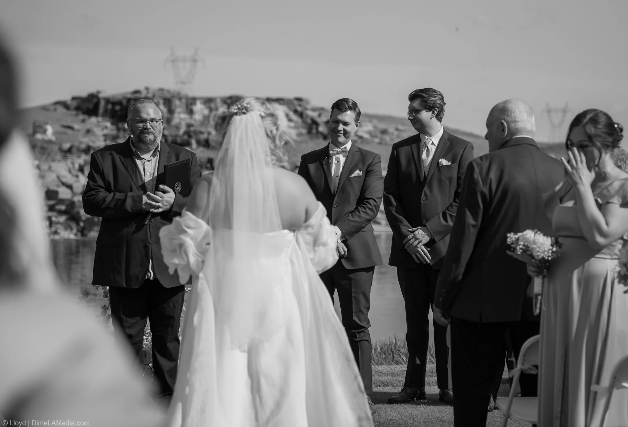 Black and white wide view of the ceremony with the wedding party and guests looking on