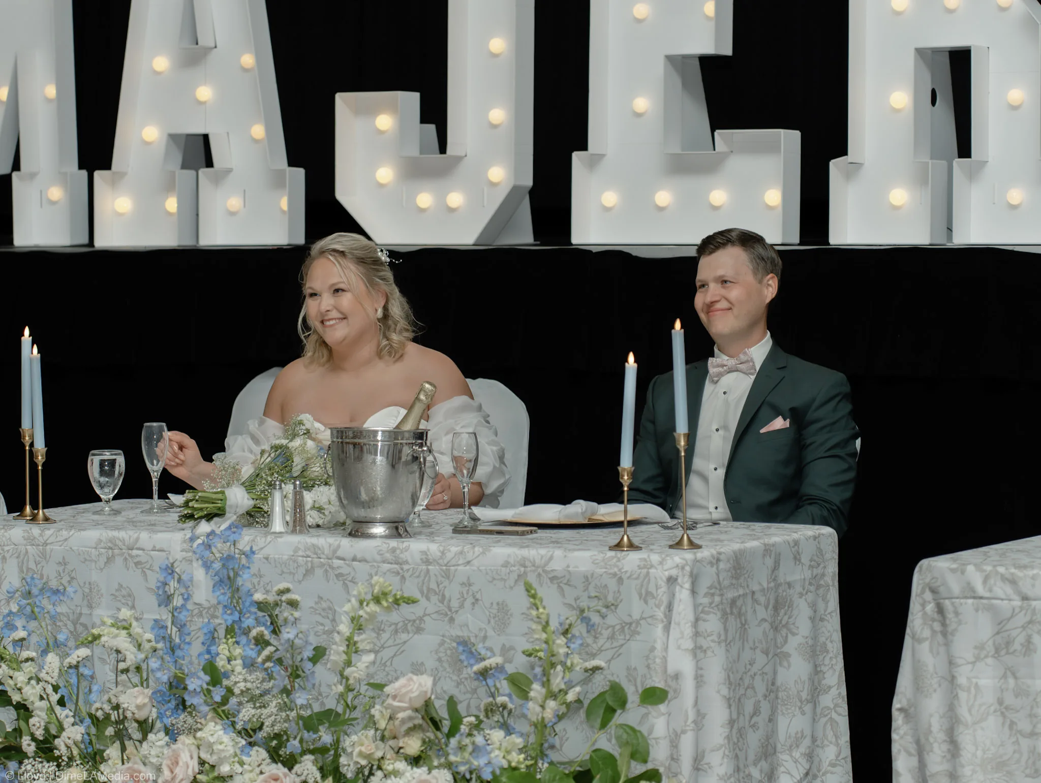 Bride and groom at the head table beneath lit marquee letters at their reception