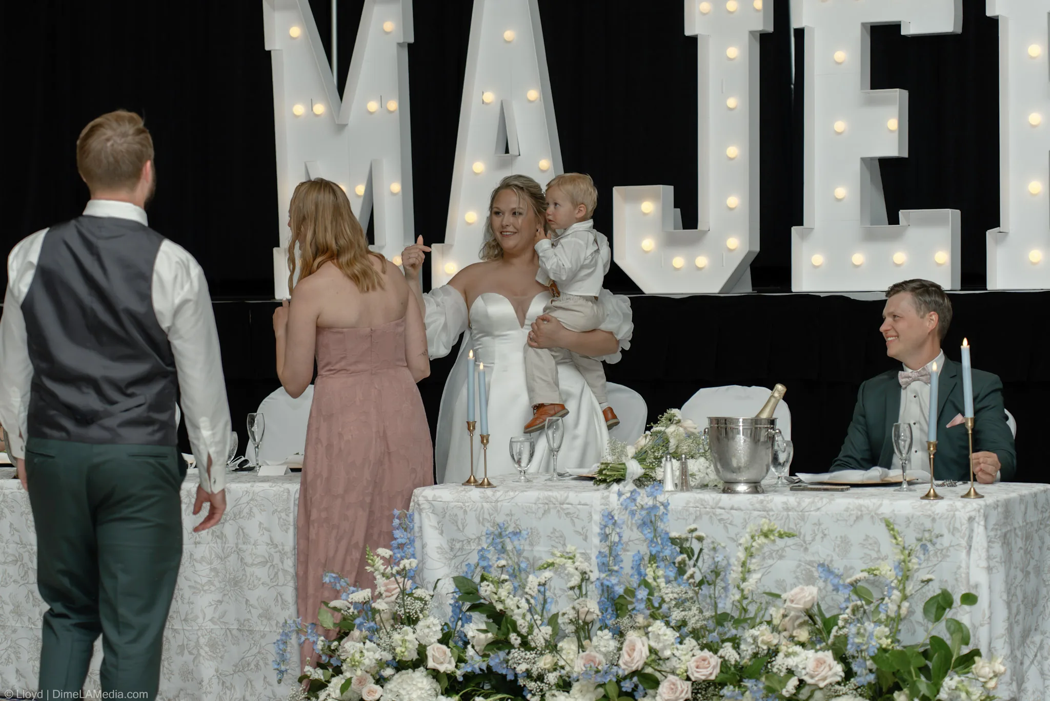 Reception head table with the bride holding a toddler while guests come over to talk