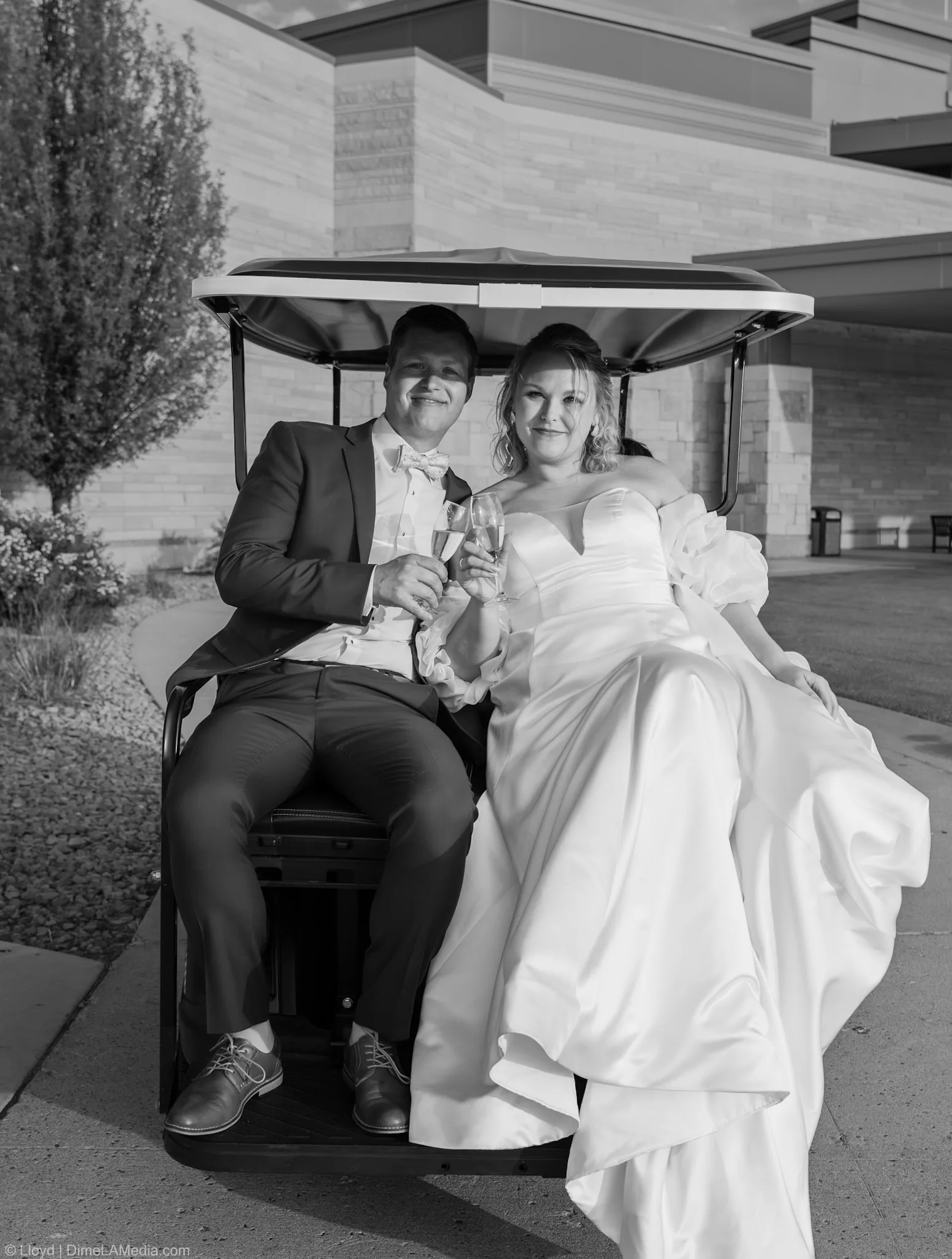 Black and white photo of a bride and groom toasting champagne in a golf cart in their wedding clothes