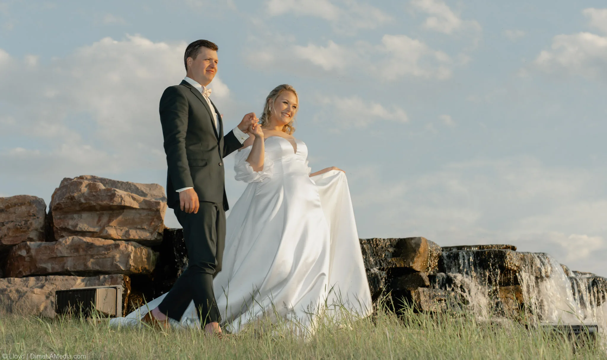 Bride and groom walking together past the quarry waterfall in the evening light