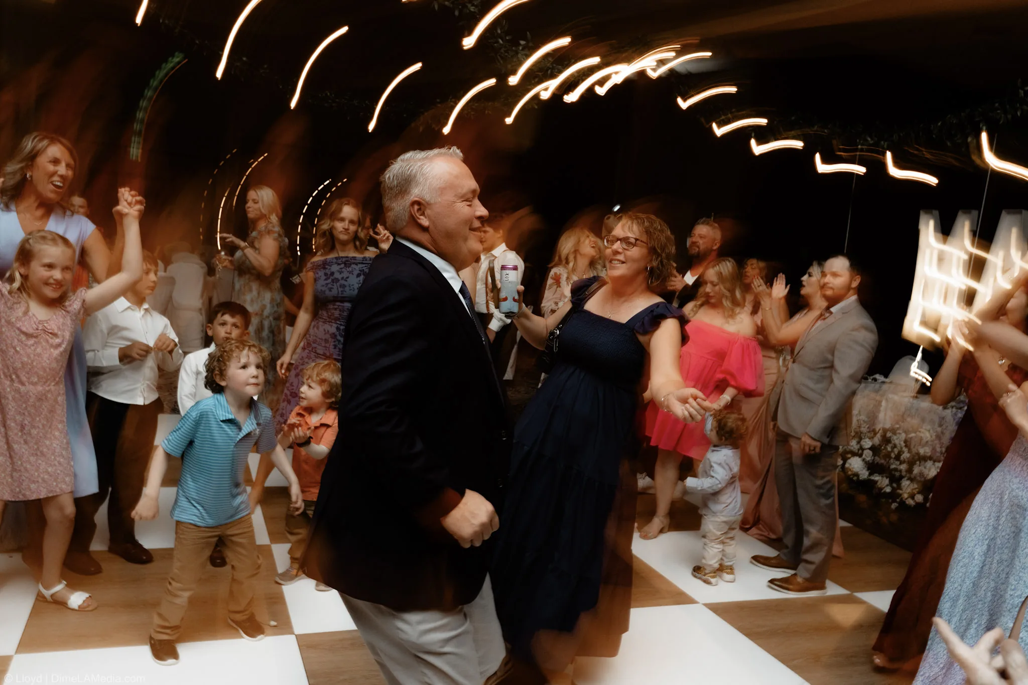 Packed wedding dance floor in motion under streaking string lights