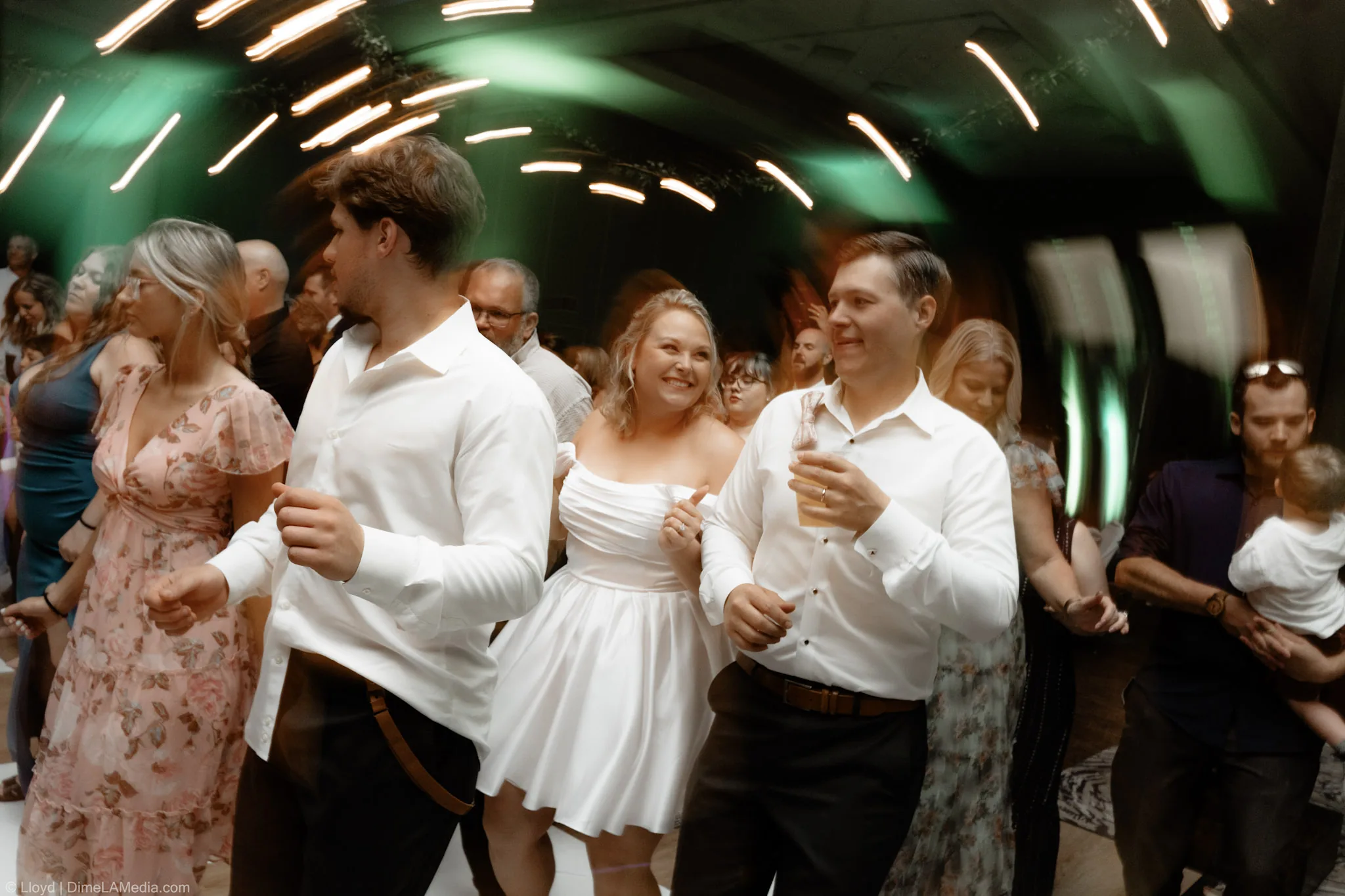Bride in her short reception dress dancing in the middle of the crowd under green light