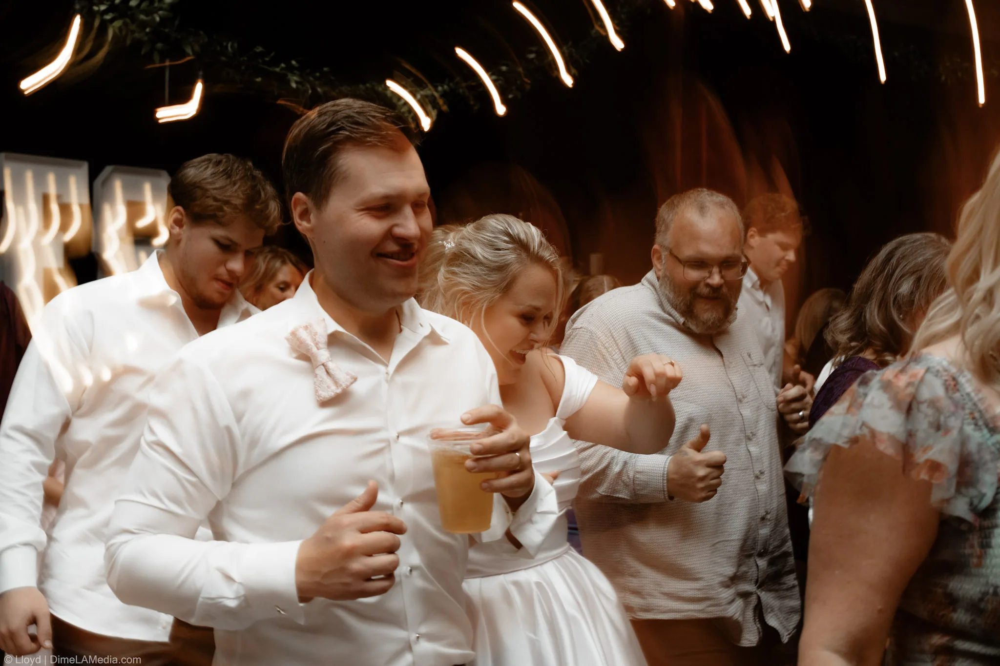 Bride and groom dancing with friends late in the reception, drinks in hand