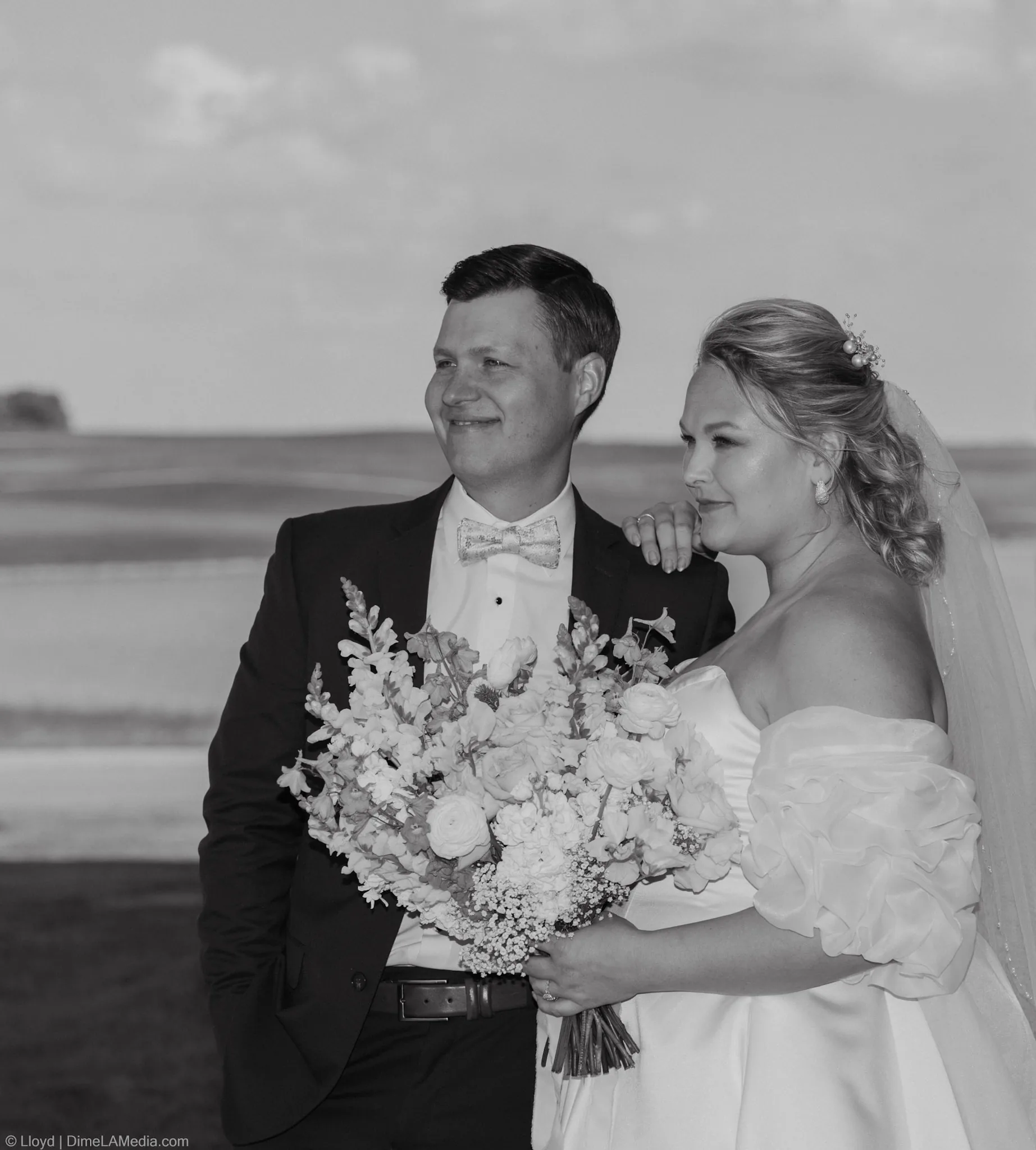 Black and white portrait of a bride and groom standing together behind her bouquet