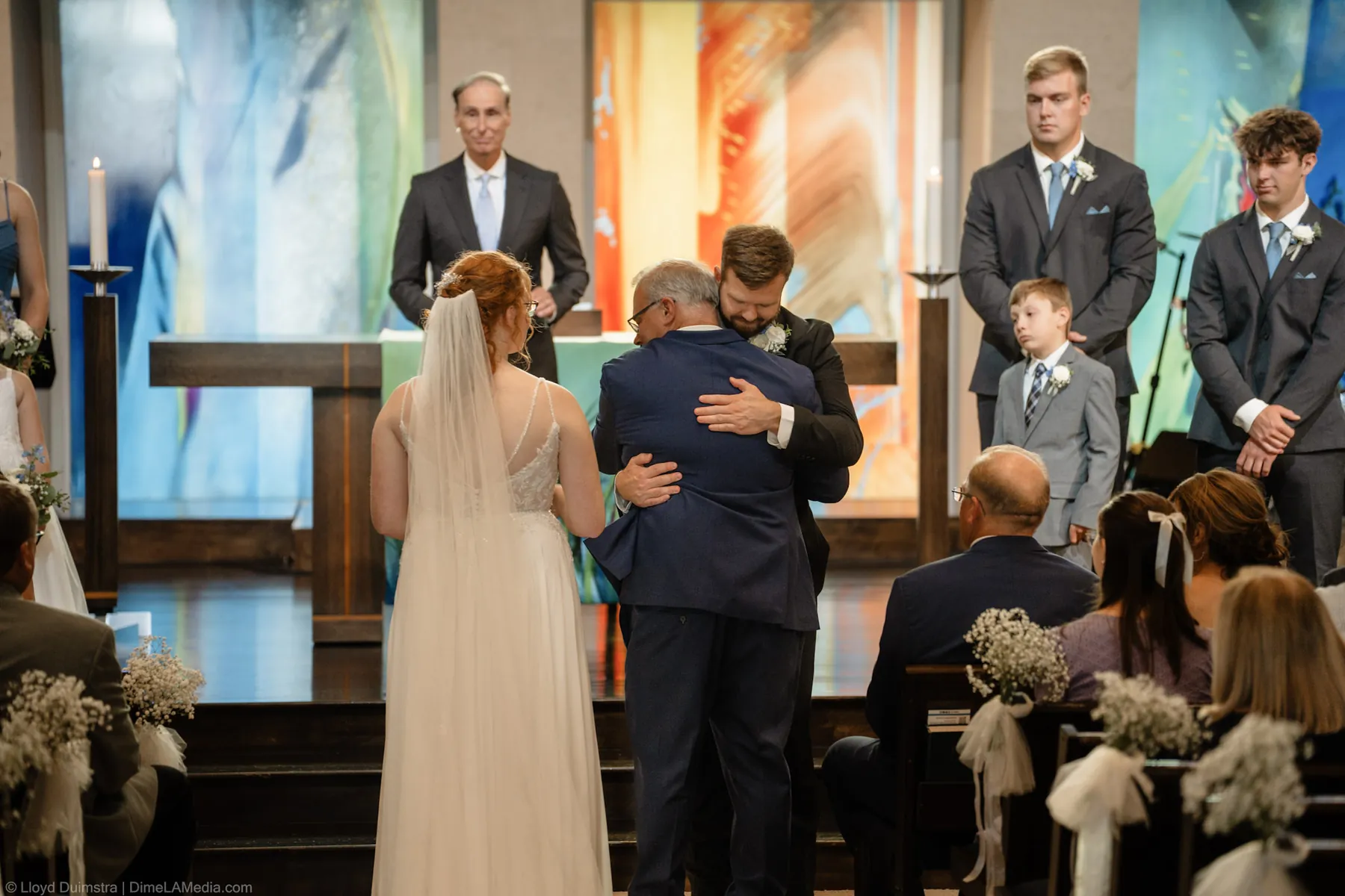 Bride and groom embrace at the altar in front of the wedding party